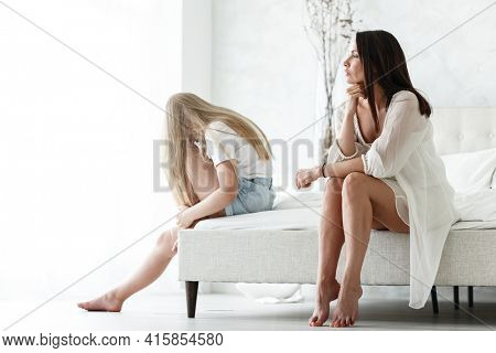 Family conflict and relations concept. Mother and daughter having quarrel and aguring at home. Sad woman and teenage girl sitting on bed. Not looking at each other.