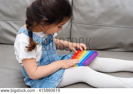 Young Little Girl Sitting On The Sofa At Home Playing Poppit-new Fidget Toy, Popular With Kids, Help