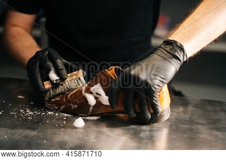 Close-up Hands Of Unrecognizable Shoemaker In Black Gloves Applying Cleaning Foam On Old Light Brown
