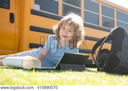 Pupil Writing Homework On Grass With Tablet Outdoor Near School Bus