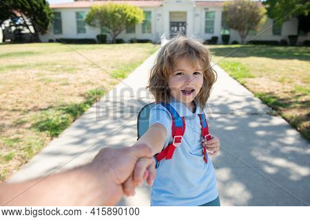 Pupil Holding Parent Fathers Hand On Blurred School Building Background. Child With Rucksacks Standi