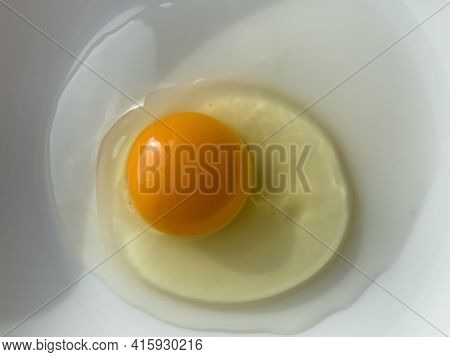 One bright yellow raw chicken egg in a white bowl.