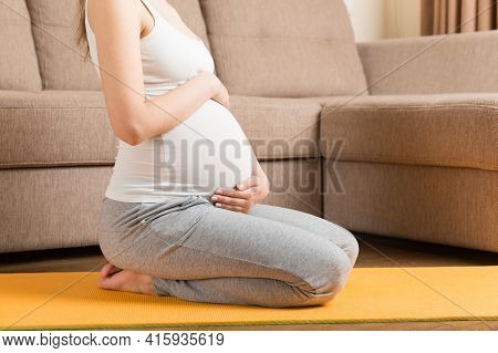 Beautiful Young Pregnant Woman Sitting On Mat In Yoga Pose At The Home. Pregnancy Yoga And Fitness C