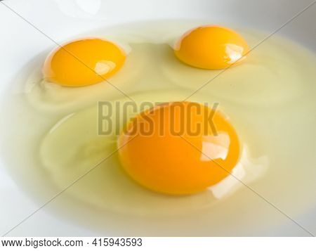 Three bright yellow raw chicken eggs in a white bowl.
