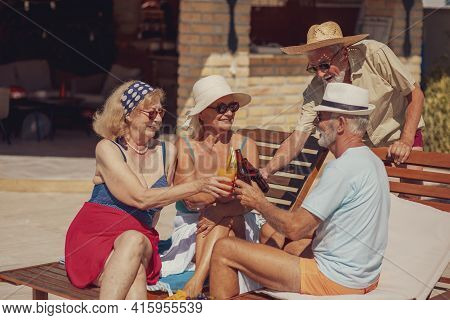 Group Of Senior Friends Relaxing And Sunbathing On Sun Beds By The Swimming Pool While On A Summer V