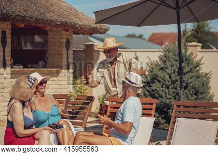 Group Of Senior Friends Relaxing And Sunbathing On Sun Beds By The Swimming Pool While On A Summer V