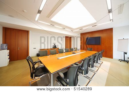 Long wooden table, black armchairs in light room for business meetings. 
