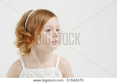 Little beautiful red hair girl in white dress looks away on grey background.