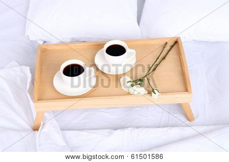 Cups of coffee on comfortable soft bed with pillows