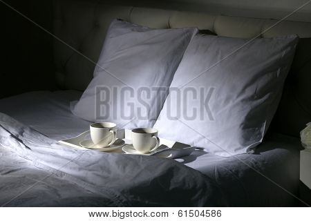 Cups of coffee on comfortable soft bed with pillows