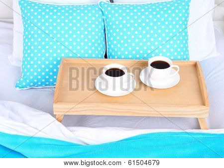 Cups of coffee on comfortable soft bed with pillows