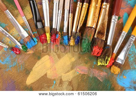 Many brushes in paints on multicolor wooden background