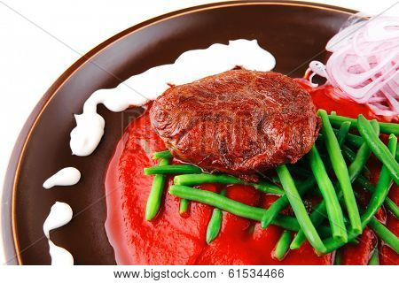pork medallion served on tomato sauce with green peas on dark plate isolated on white background
