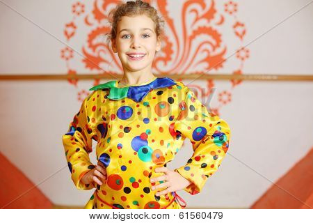 Beautiful girl dressed as jester poses and smiles near wall with pattern