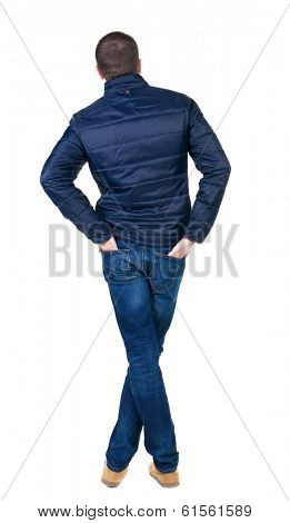 Back view of handsome man in blue windcheater looking. Standing young guy in jeans. Rear view people collection.  backside view of person.  Isolated over white background.
