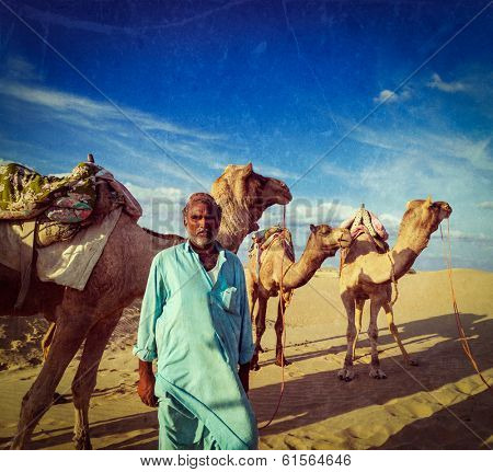 Vintage retro hipster style travel image of Rajasthan travel background Indian man cameleer (camel driver) portrait with camels in Thar desert with grunge texture overlaid. Jaisalmer, Rajasthan, India