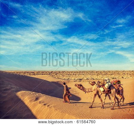 Vintage retro hipster style travel image of Rajasthan travel background - India cameleer (camel driver) with camels in dunes of Thar desert with grunge texture overlaid. Jaisalmer, Rajasthan, India