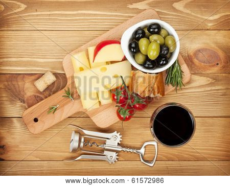 Red wine with cheese, bread, olives and spices. Over wooden table background. View from above