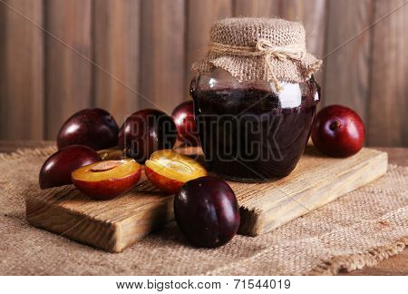 Tasty plum jam in jar and plums on wooden table close-up