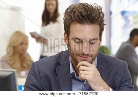 Young businessman thinking in office hand on chin, looking down.
