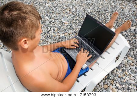 Man Reclining On Chaise Lounges op Beach, op zoek In laptop