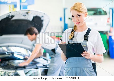 Male and female mechanic team examine car engine with light and checklist in workshop 