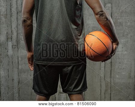 Afro-american basketball player holding the ball at his side