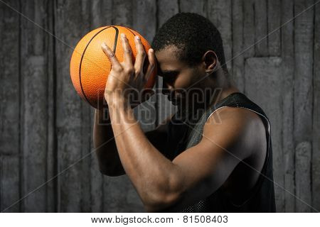 Afro-american basketball player pressing ball to his forehead