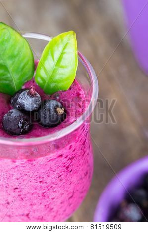 Milkshake with black currants in a glass against the background of wooden boards