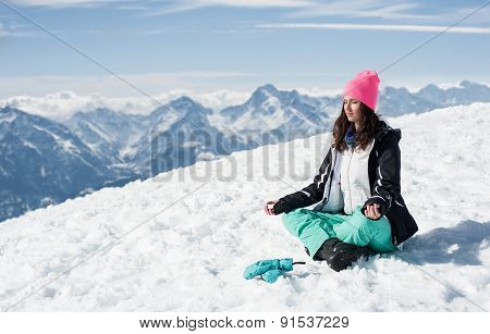 Beautiful young woman doing yoga in the snow mountains
