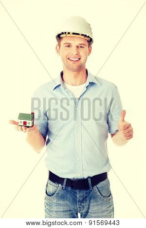 A forewoman holding a model house in hand and gesturing OK