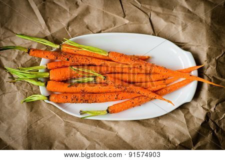 Oven-baked Baby Carrots Sprinkled With Fresh-grounded Black Pepper On White Plate On Craft Paper