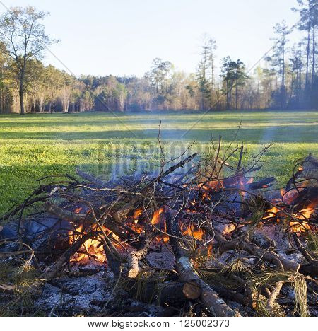 Pile of brush in a green field that is being burned