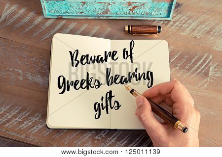 Retro effect and toned image of a woman hand writing on a notebook. Handwritten quote Beware of Greeks bearing gifts as inspirational concept image