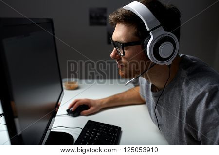 technology, gaming, entertainment, let's play and people concept - young man in headset and glasses with pc computer playing game at home and streaming playthrough or walkthrough video
