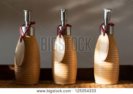 beauty, body care, luxury, natural cosmetics and hygiene concept - close up of liquid soap or body lotion set with blank  wooden nameplates at hotel bathroom