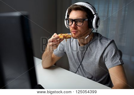 technology, gaming, entertainment, let's play and people concept - young man in headset with pc computer eating pizza while playing game at home and streaming playthrough or walkthrough video