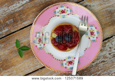 Crunchy and creamy tartelette with raspberries and blueberries on pink plate rustic wooden surface