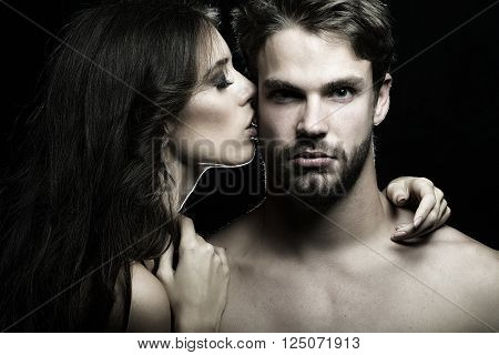 Closeup portrait of young beautiful sexual couple of brunette woman with long hair embracing and kissing handsome muscular man in studio on black background horizontal picture