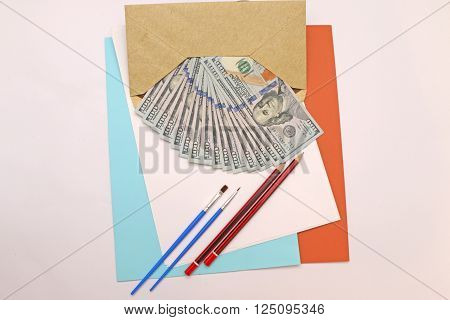 dollar bills folded in an envelope with paper and beside it lay pipes and pencils to color in.