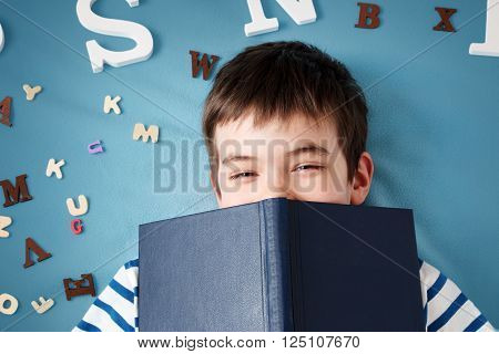 seven years old child lying with book and letters on blue background