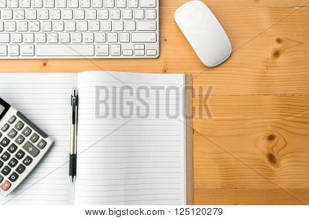 Top view workspace with blank notebookpencalculator keyboard and mouse on wooden table background.