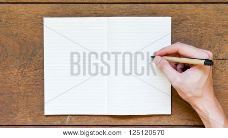 Man hands with pen writing on empty notepad over wooden table.