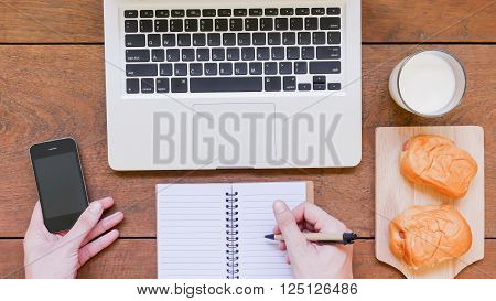 Laptop, notebook, mobile phone and breakfast on wooden table background.