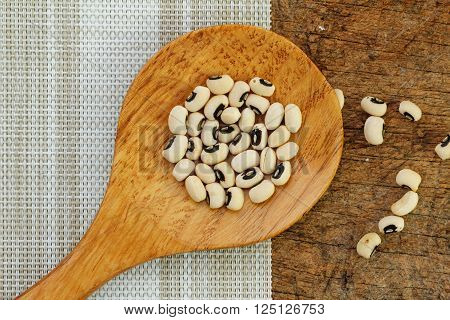Black eye peas in wooden spoon on textured background