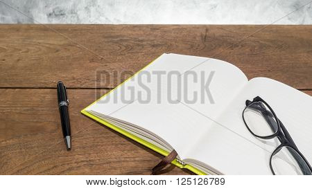 Blank notebook with pen and glasses on wooden table.