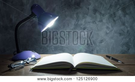 Lamp with notebook, pen and glasses on wooden table with vintage wall background.