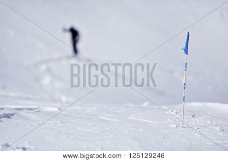 Blue flag blown by the wind on a mountain in winter and skier in background