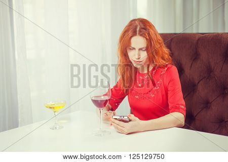 Beautiful girl talking on the phone in a cafe and drink wine.