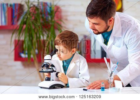 teacher helps kid to conduct experiment with microscope in school lab